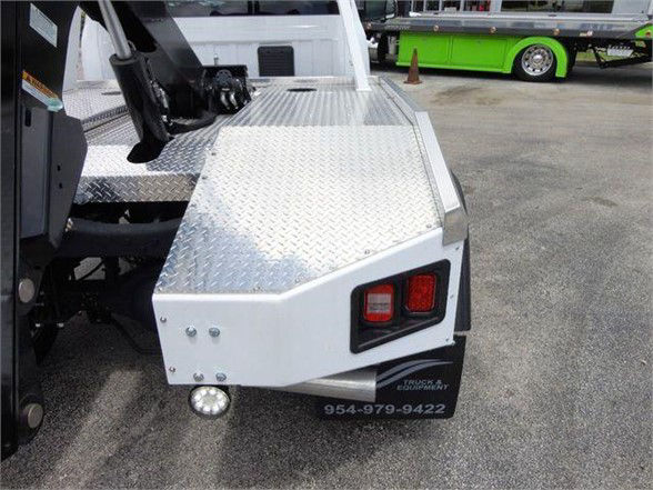 Ram 4500 SLT tow truck rear body with diamond plate platform and rectangular taillight, plate bracket with phone number visible.
