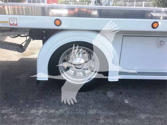 Peterbilt 337 tow truck side view showing wheel well and chrome wheel. Small warning sticker and side cabinet visible.