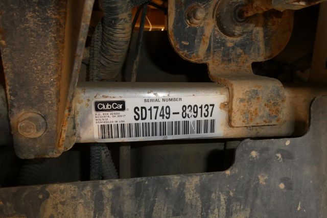 Club Car serial label showing SD1749-830137 on a metal surface, with surrounding dirt and machinery components.