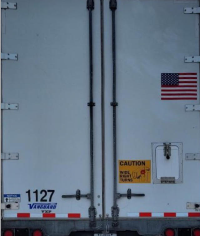 Rear of a 2019 Vanguard VXP trailer with double rear doors, US flag decal, stock number 1127, CAUTION sticker, and VIN/stock details visible.