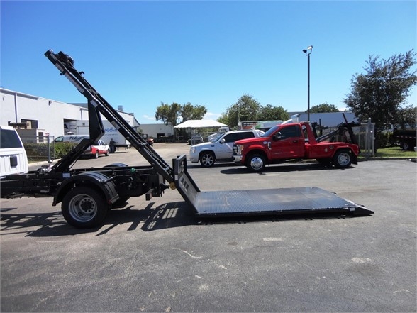 Ram 5500 HD hooklift truck with a raised loader arm and flatbed at a dealership lot.