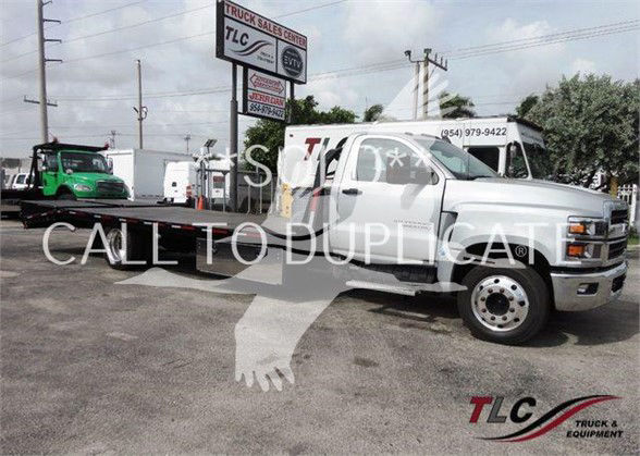 2023 Chevrolet Silverado 6500HD flatbed tow truck with extended cab, silver exterior, and flatbed body parked at dealership lot.