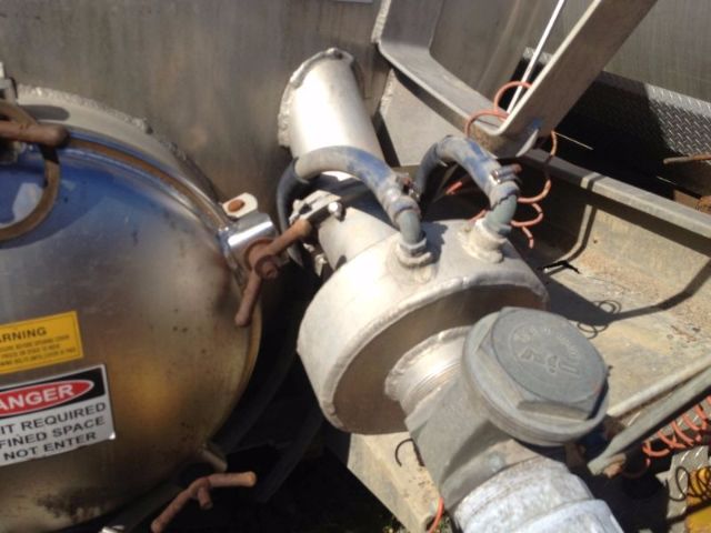 Truck vacuum tank equipped with hoses and caps showing a cylindrical pressure vessel and valve assembly, metal piping, and warning label on a round tank.