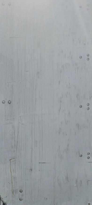 Image shows a weathered light-gray trailer side panel with multiple rivets and subtle vertical streaks.