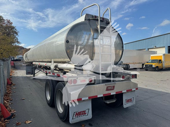 Tank trailer with cylindrical metal tank mounted on dual-axle chassis, rear view showing pumping/line-off area, HEIL branding on mud flaps.