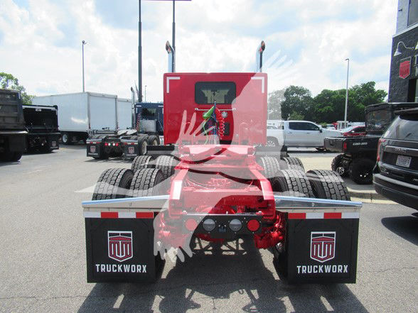 Rear view of a red Kenworth W990 truck chassis with fifth wheel and dual rear axles; black mudflaps labeled 'TRUCKWORX' on both sides.