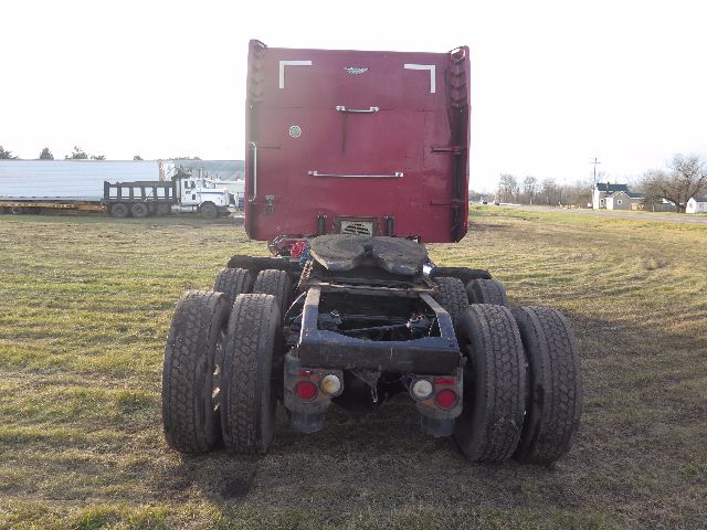 Peterbilt 388 tractor rear view showing chassis, dual rear axles, and fifth-wheel area with maroon cab in background.
