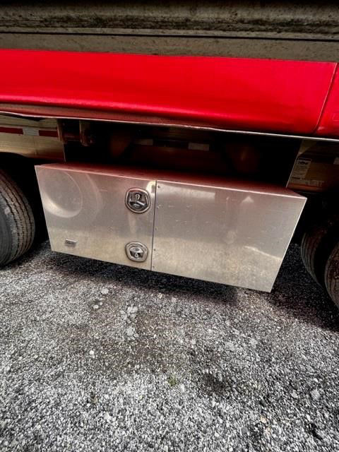 Aluminum storage toolbox mounted under side of a red curtainside trailer, with two circular lockable latches.