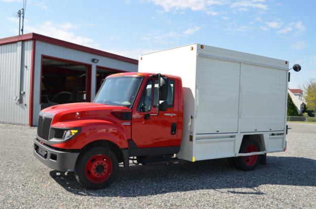 2013 International TerraStar medium-duty truck with red cab and white service body, parked on gravel near a building.
