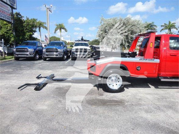 Tow truck with red Ram 4500 front and frame extending a towing apparatus in front of other trucks; dealership lot in background.