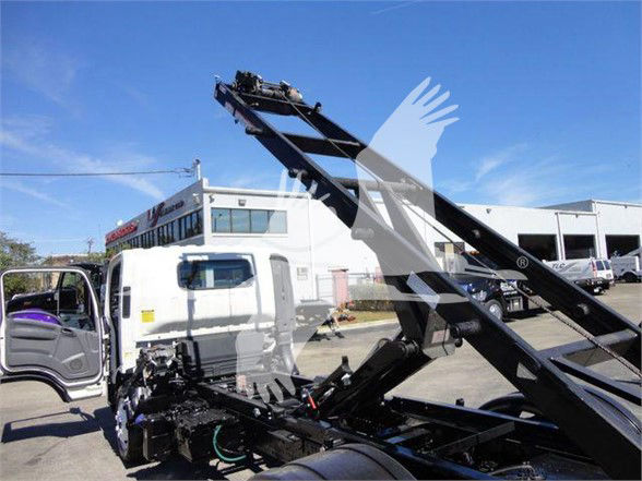 Isuzu NRR truck with a hydraulic lift/roll-off in a vehicle lot, cab open, side view showing loading apparatus.