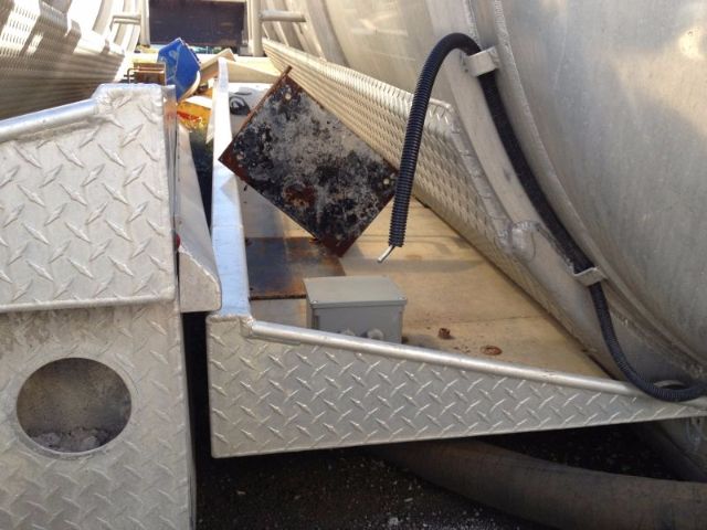 Vacuum Tank trailer side showing diamond plate steel, hoses, and a small gray toolbox with a black corrugated hose nearby.