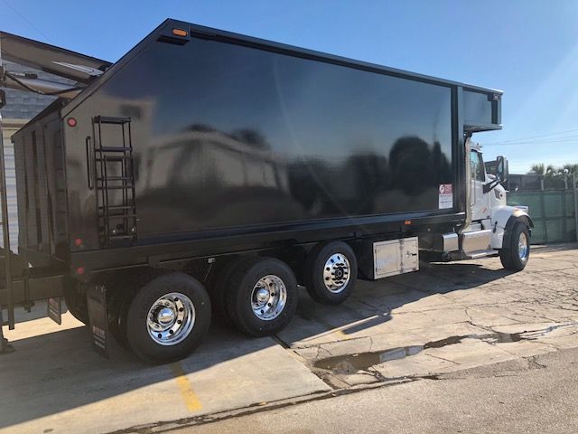 2018 Peterbilt 567 grapple truck side view showing long black dump bed and dual rear axles with chrome wheels.
