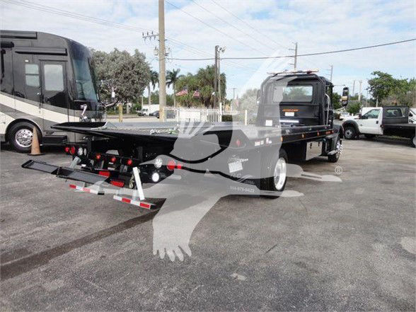 Tow truck with flatbed and hydraulic lift showing rear equipment, tail lights, and support frame. Text on components partially visible: no legible model numbers clearly readable.