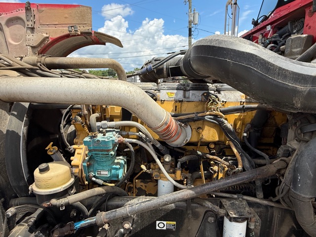 Peterbilt 379 engine bay showing exhaust manifold, turbo piping, hydraulic hoses, and engine block with yellow paint.