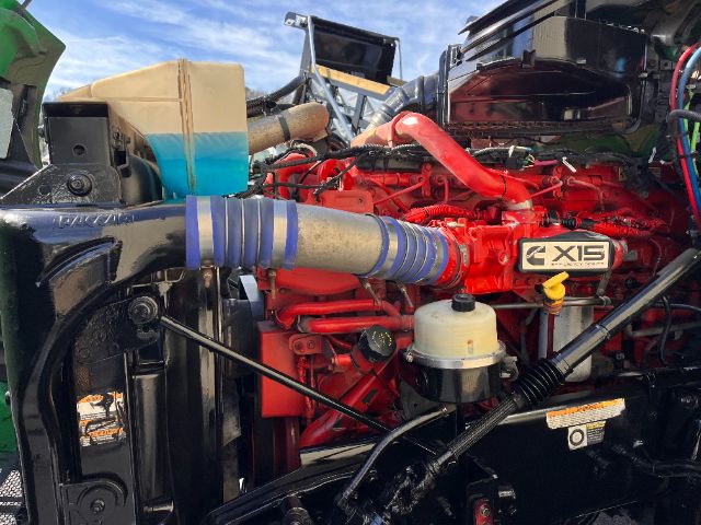 Truck engine bay with bright red engine labeled X15 and blue flexible intake hose; surrounding hoses, reservoir, and components visible.
