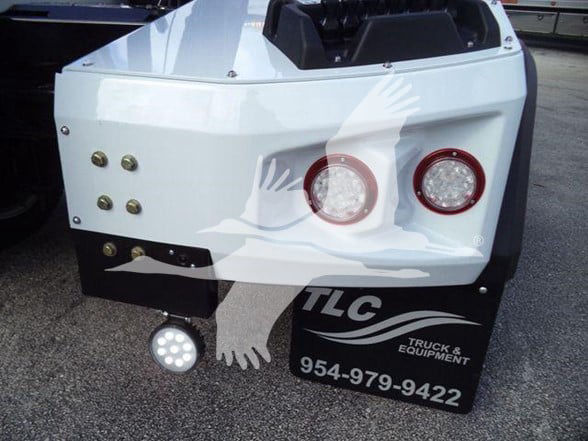 Rear of a 2023 Chevrolet Silverado 6500HD tow truck showing white body panels, two circular red taillights, and a black mudguard with TLC Truck & Equipment logo and phone number 954-979-9422.