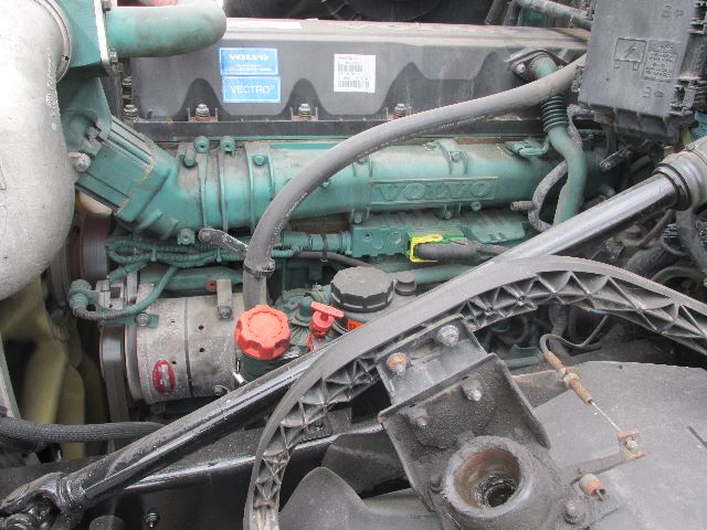 Volvo engine bay showing green Volvo engine with orange oil cap and red fuel cap, surrounding hoses and belts in a truck engine compartment.