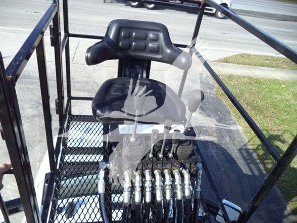 Cockpit and control levers of a heavy equipment truck, hydraulic hoses visible, seating with backrest, metal frame surrounding operator area.