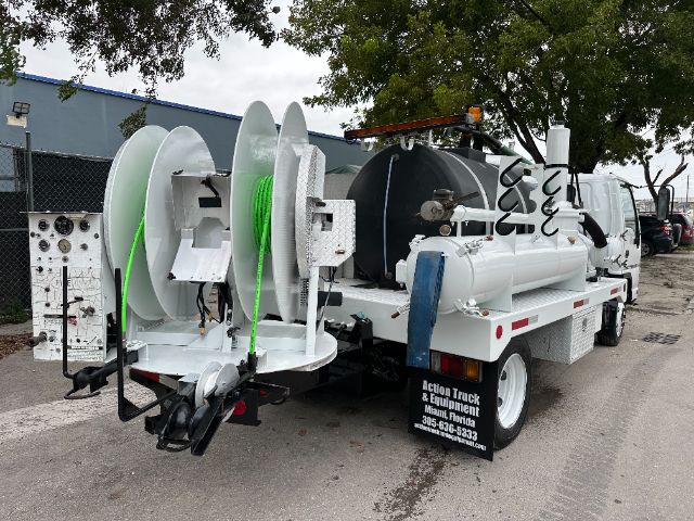 Rear view of a white GMC W5500 vacuum truck with large reels for hoses, tank, and equipment mounted on a flatbed. Visible text includes a sign on the side reading 'Action Truck & Equipment Mims Florida' and phone number.