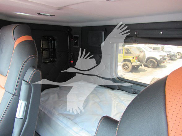 Interior of a new Kenworth W990 sleeper cab showing bed with light blue bedding and black/orange seats.