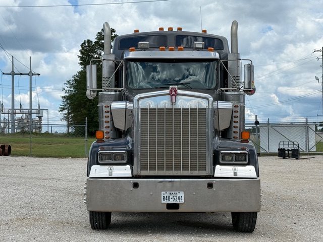 Front view of a 2012 Kenworth W900 conventional sleeper truck with chrome grille, large bumper, and dual antennas.