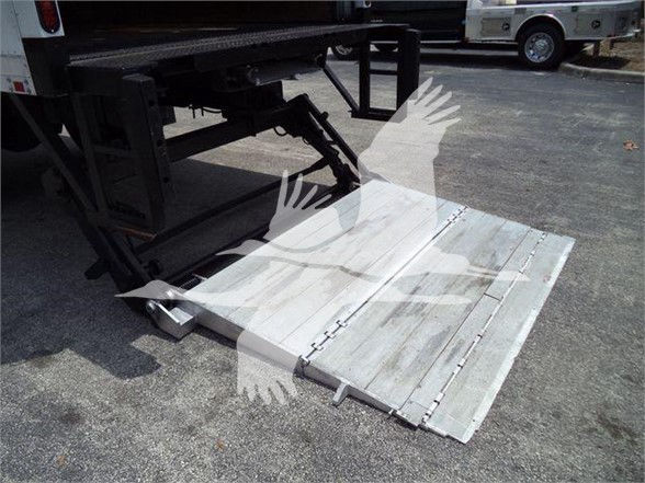 Truck wheelchair lift platform or ramp folded under a Mack MD7 truck showing metal ramp with hinges and hydraulic support.