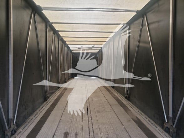  Trailer interior showing aluminum base rails and side curtains with a wooden floor inside a flatbed trailer.