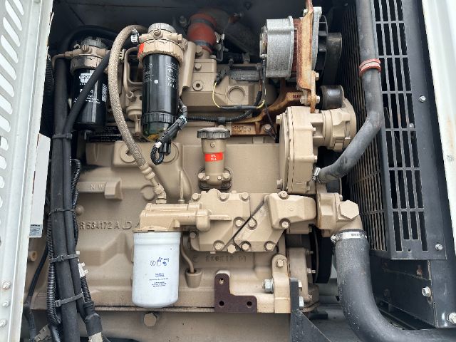 Engine bay of a 2014 Freightliner 114SD showing a diesel engine with oil filter, fuel filter, hoses, belts, radiator fan, and exhaust components. Visible labels include a red tag on a component and a white cubic filter housing.