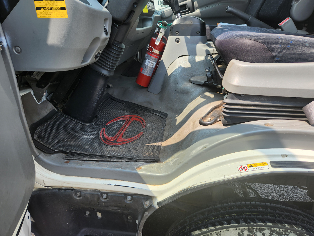 Cab interior of 2017 Hino 155 showing driver floor mat with logo, fire extinguisher, center console, and yellow caution sticker near door.