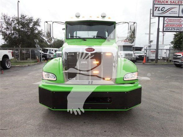 Peterbilt 337 truck front view with bright green cab and chrome grille, stock image with watermark and dealership lot in background.