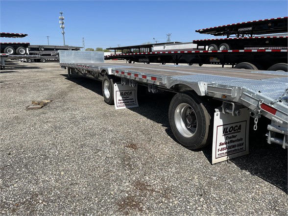 Manac steel stepdeck trailer in an outdoor lot with other trailers; visible text on mud flaps reads LOCA Trailers and contact numbers.