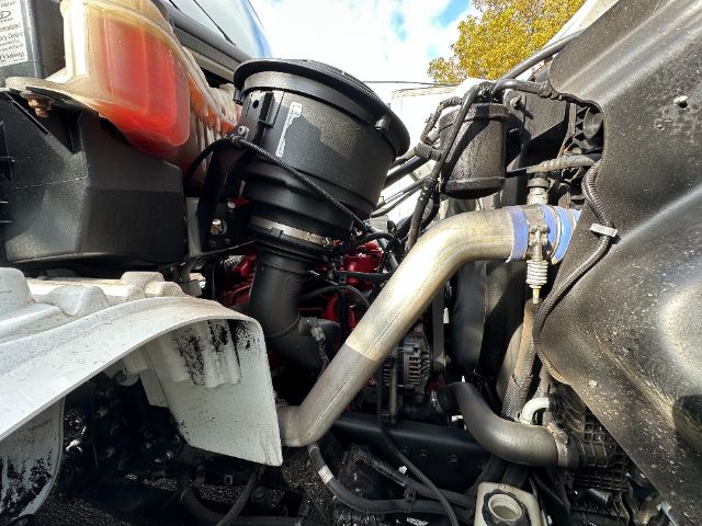 Freightliner M2 engine bay showing air intake, coolant hoses, and radiator area with metal tubing and wiring visible.