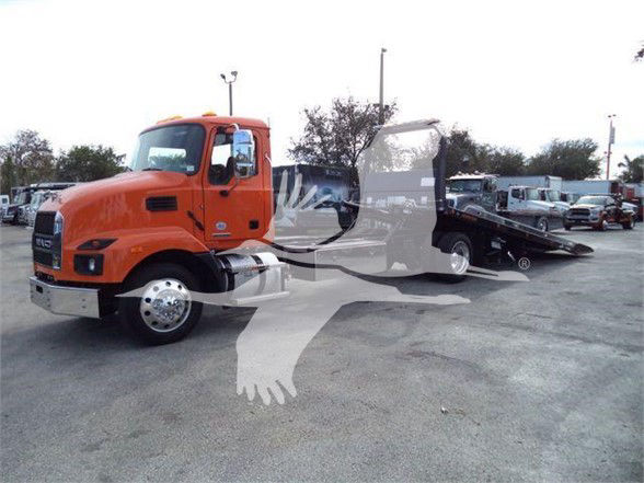 Orange 2024 Mack MD6 tow truck with a flatbed in a dealership lot.