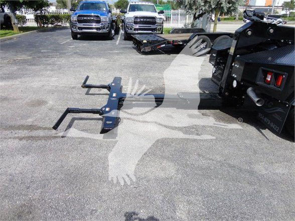 Ram 4500 tow truck with hitch attachment in foreground and two Ram trucks in lot in background.