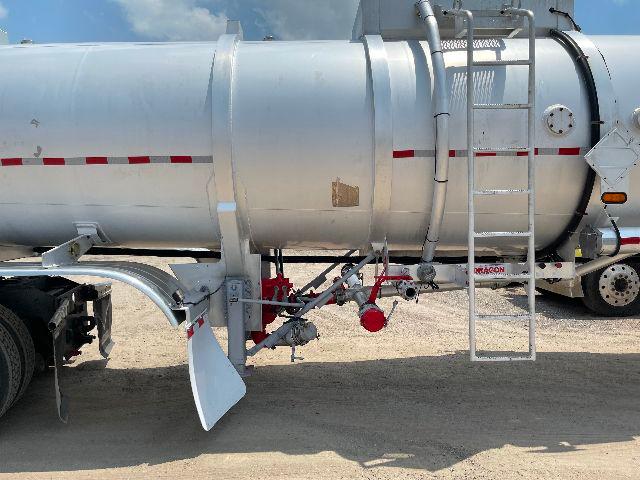Trailer underside showing cylindrical aluminum crude oil tanker with ladder and piping. Visible text includes a small label on the tank and a decal near the rear axle.