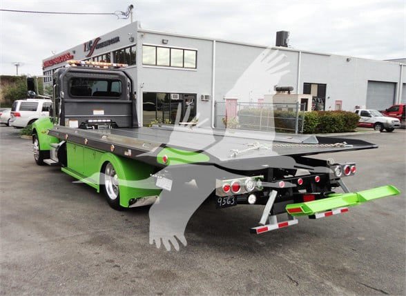 Peterbilt 337 tow truck with a bright green and black color scheme, flatbed tow equipment, rear view showing multiple lighting and hook components.