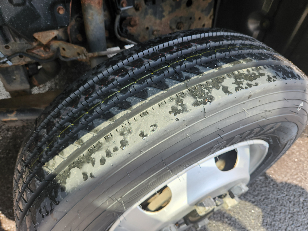Truck front wheel and fender with tire and wheel well showing rubber and metal components.