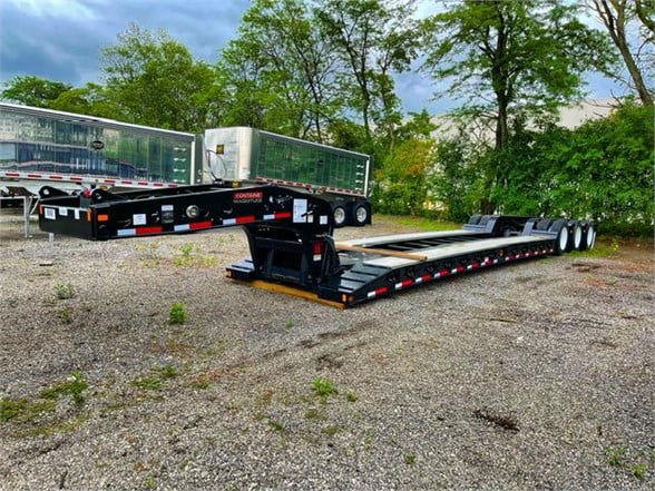 Fontaine semi-trailer with double drop deck lowboy layout, black frame, multiple axles, resting on a gravel lot with trees in the background.