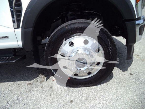 Wheel front tire and hub of a 2024 Ford F-450 with chrome wheel and black fender. Partial truck body visible.