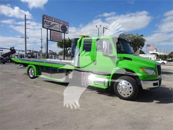 2024 International MV tow truck with bright green and gray color scheme, flatbed, side view, dealership lot in background