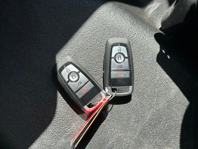 Two Ford remote key fobs with buttons for lock, unlock, and a red key tag resting on a textured surface.