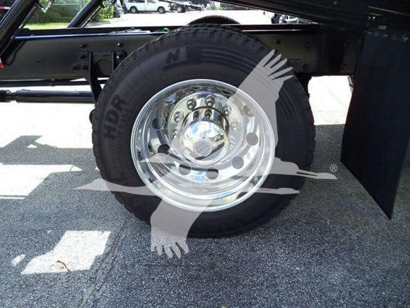 Wheel and tire assembly on a truck with chrome rim and heavy-duty tire; faint text 'NORD' on tire sidewall and a watermark graphic across the image.
