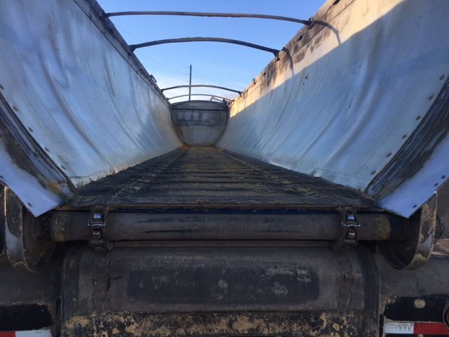 Trailer bed interior with metal sidewalls and roller hinges; dirt and wear on bed surface, rear axle area visible.