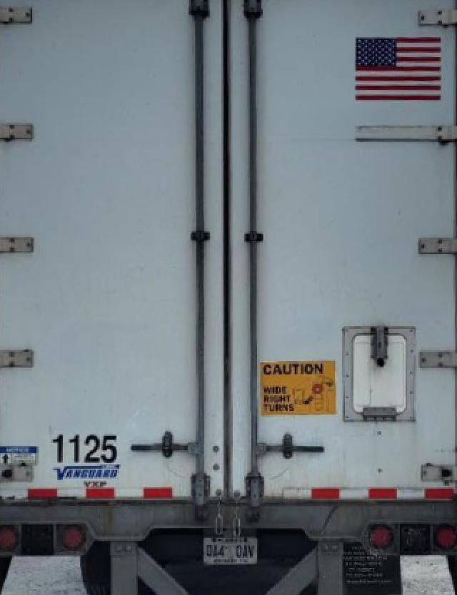 Rear of a 2019 Vanguard VXP utility trailer with two vertical doors, US flag sticker, yellow caution label, stock number 1125, VIN partially visible, and bumper with lights.