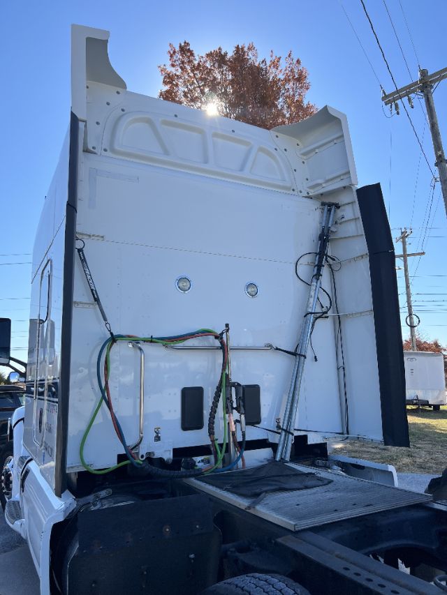 Peterbilt 579 rear sleeper cab area with visible electrical lines, hoses, and battery box mounted on white back of cab.