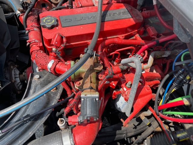 Engine bay of a 2013 Freightliner M2 with a red 6-cylinder engine, visible hoses, wiring, and components in a sewer service truck.