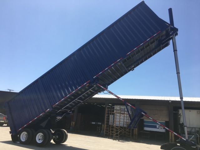 Blue 40 ft dump trailer raised at angle with hydraulic ram and tandem axle, side walls visible, loading area open.