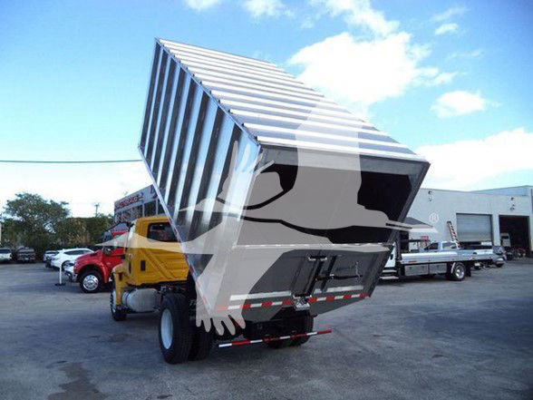 2019 International DURASTAR 4300 chassis with a raised dump bed in a yard, yellow truck cab with other equipment in background.