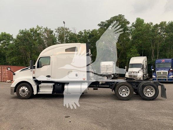 Kenworth T680 tractor in a side view, white cab, with a rear chassis and multiple axles; vehicles in background.